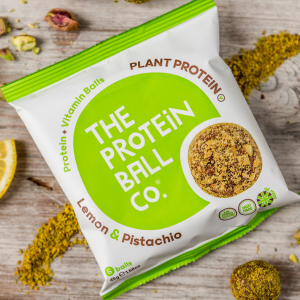 A Protein Ball Co pack surrounded by grounded pistachio
